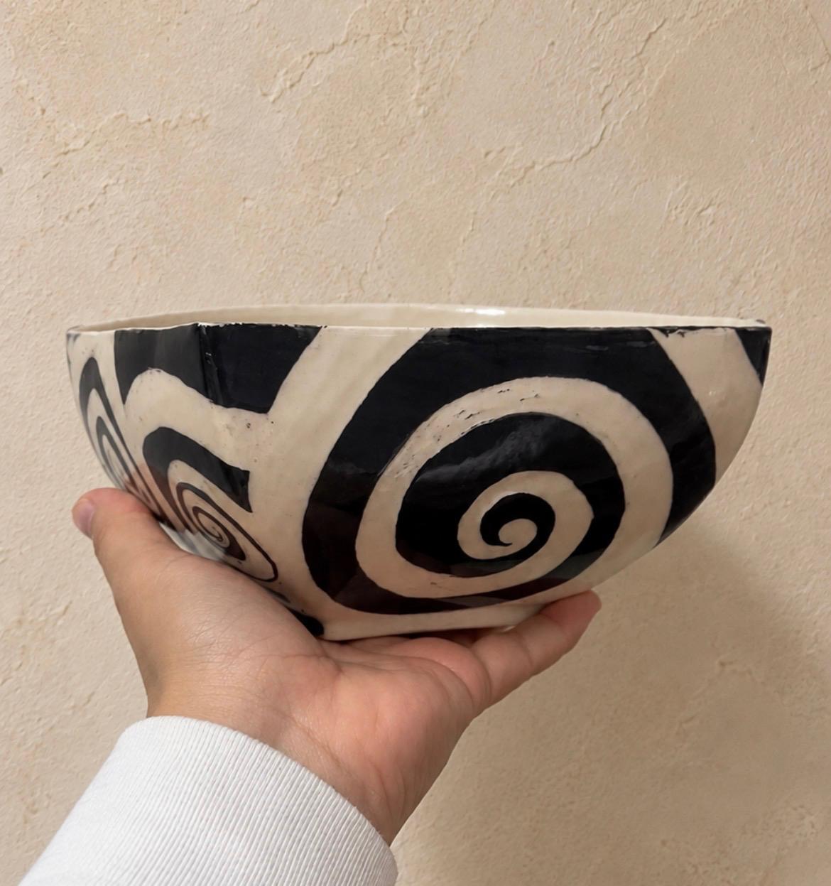 Bowl de cerámica UGA con espiral en blanco y negro, sostenido en la mano